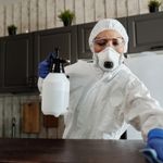 Manipulador de alimentos con mascarilla y guantes desinfectando una superficie de trabajo en una cocina profesional.